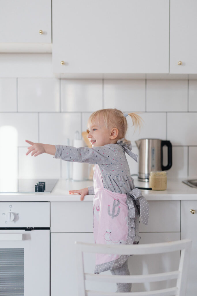child standing on chair near electric cooktop